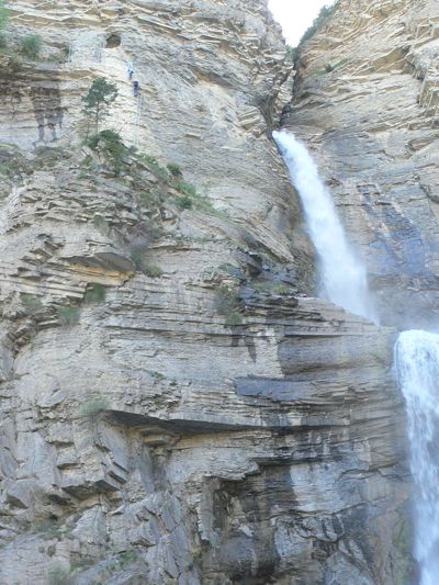 La cascada baja con fuerza en época de deshielo. Al costado se puede ver gente accediendo a la cueva 